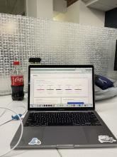 Laptop open in front of opalescent tile wall. Partially finish bottle of soda on left.