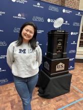 Woman stands with U-M Natty trophy from 2024.
