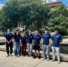 Seven students stand in front of the Triton fountain on Ingalls Mall in Block M ts.